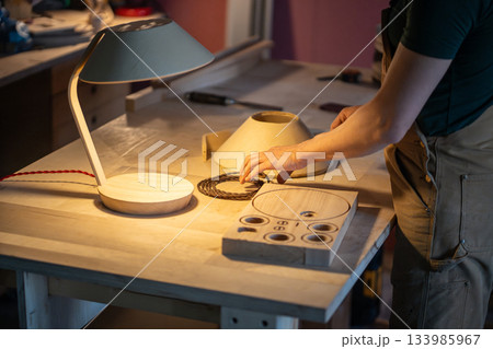 Man carpenter manufacturing wooden lamp in carpentry workshop, choosing wire for furniture object. 133985967
