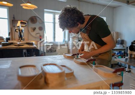 Man carpenter blowing dust and sawdust off wooden coasters for water glasses, workshop process. Man carpenter blowing dust and sawdust off wooden coasters for water glasses, workshop process. 133985980