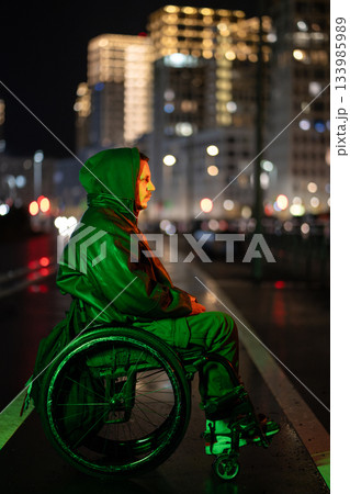 Pondering disabled man in wheelchair in green neon rgb light in deep thinking on late night walk. 133985989