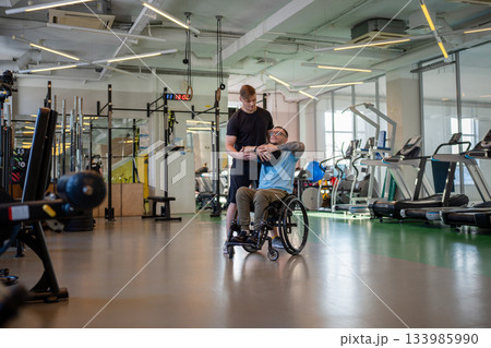 Man athlete in wheelchair working out with medicine ball at training session with professional coach 133985990