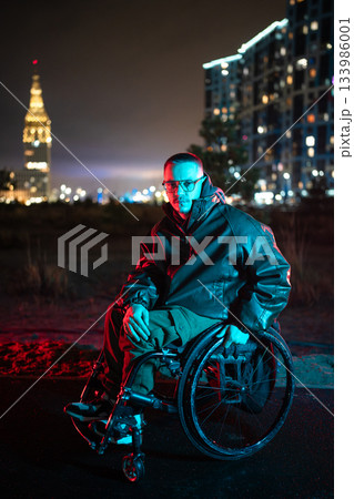 Disabled man in wheelchair in blue red neon rgb color light walking late outdoors, staying healthy. Disabled man in wheelchair in blue red neon rgb color light walking late outdoors, staying healthy. 133986001