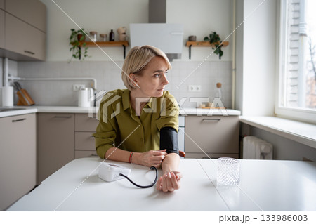 Sick tired middle aged woman measuring blood pressure level with tonometer, seasonal health issues. Sick tired middle aged woman measuring blood pressure level with tonometer, seasonal health issues. 133986003
