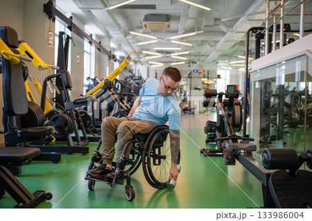 Disabled man in wheelchair at sports center using dumbbell to build upper body and arms strength. 133986004