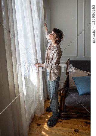 Calm woman removing curtains for laundry and home decor update on weekend day, household chores 133986162