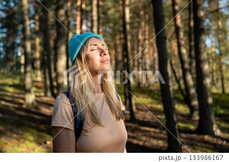 Female traveler enjoying sun through trees taking break on woodland trail. Peaceful forest hiking 133986167