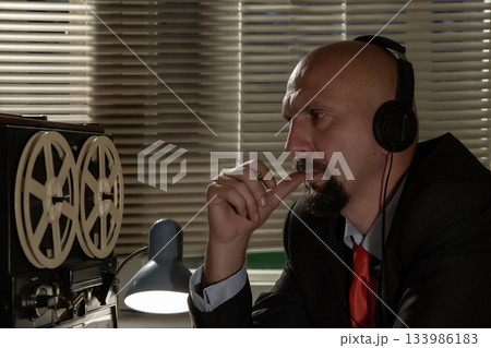Bald man in headphones listening to music, listening and recording conversations, watching and controlling people, the average plan 133986183