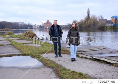father and daughter are walking in the cold season near the lake in autumn, early winter, puddles 133987190