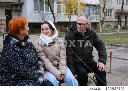 Grandfather, grandmother and granddaughter walking down the street, teenage girl in a brown coat, bald man and woman with red hair 133987191