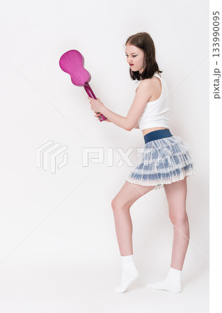 Female musician with ukulele in hands swinging musical instrument with rage and irritation, trying to break ukulele in fit of despair and emotional depression while learning to play string instrument Female musician with ukulele in hands swinging musical instrument with rage and irritation, trying to break ukulele in fit of despair and emotional depression while learning to play string instrument 133990095