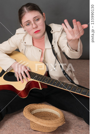 Female guitarist and street musician stretching out hand in hope of receiving donation for her musical performance. Her countenance directed towards camera, conveying sense of hope and anticipation Female guitarist and street musician stretching out hand in hope of receiving donation for her musical performance. Her countenance directed towards camera, conveying sense of hope and anticipation 133990130