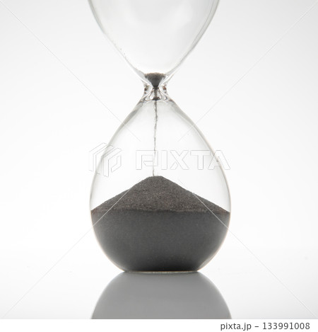 Close-up of an hourglass with dark sand falling, set against a clean white background Close-up of an hourglass with dark sand falling, set against a clean white background 133991008