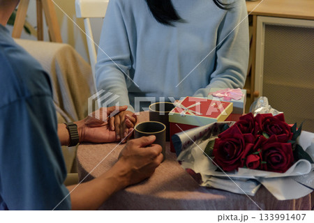Happy young couple show romantic love at home, woman and man holding hands, celebrating valentine day with gifts, red roses, cozy atmosphere, enjoying warm drinks, creating special memories. Happy young couple show romantic love at home, woman and man holding hands, celebrating valentine day with gifts, red roses, cozy atmosphere, enjoying warm drinks, creating special memories. 133991407