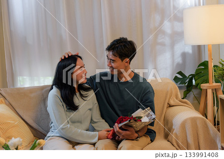 Happy young couple share tender love at cozy home, man gives woman beautiful romantic valentine day flowers, celebrating special intimate moment indoors with warm light. Happy young couple share tender love at cozy home, man gives woman beautiful romantic valentine day flowers, celebrating special intimate moment indoors with warm light. 133991408