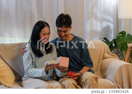 Happy young couple in love at home, woman and man exchange romantic gifts on valentine day, celebrating special connection, enjoying sweet surprise moment together indoors, embracing true affection. Happy young couple in love at home, woman and man exchange romantic gifts on valentine day, celebrating special connection, enjoying sweet surprise moment together indoors, embracing true affection. 133991426