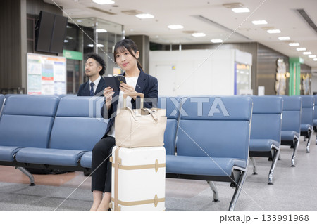 パスポートを持つターミナルで座るビジネス女性　空港や駅のターミナルでの出張移動シーン全身 133991968