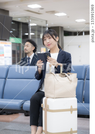 パスポートを持つターミナルで座るビジネス女性 空港や駅のターミナルでの出張移動シーン全身 パスポートを持つターミナルで座るビジネス女性 空港や駅のターミナルでの出張移動シーン全身 133991969