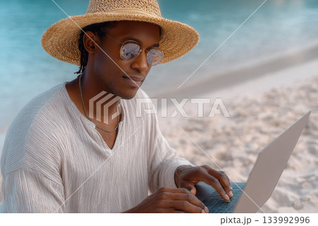 Young man working laptop beach wearing straw hat and sunglasses 133992996