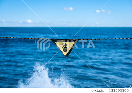 波しぶきが上がる海を背景に掲げられた注意サイン 133993509