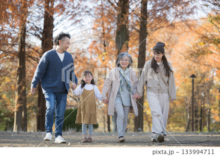 秋の家族写真・紅葉の森で笑顔の三世代家族　祖母と手を繋ぐ歩く孫と子供夫婦 133994711