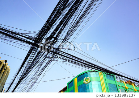 町中の交差点の頭上に重なるようにして張り巡らされている電線 133995137