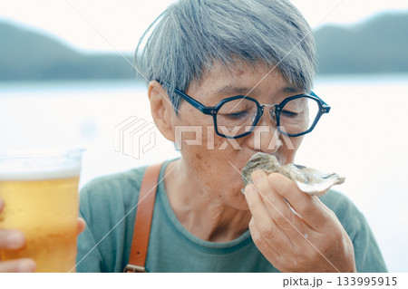 シニア女性が海辺でビールと牡蠣を楽しむシーン 133995915