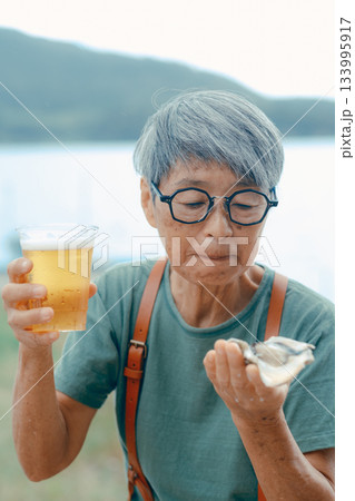 シニア女性が海辺でビールと牡蠣を楽しむシーン 133995917