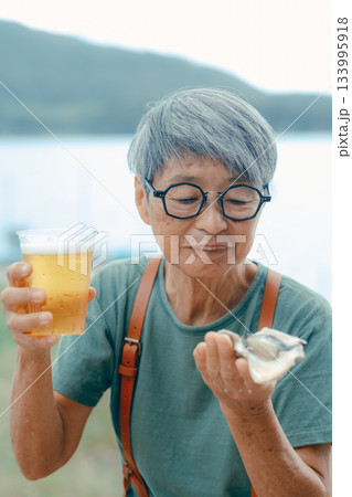 シニア女性が海辺でビールと牡蠣を楽しむシーン 133995918