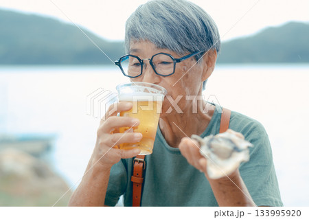シニア女性が海辺でビールと牡蠣を楽しむシーン シニア女性が海辺でビールと牡蠣を楽しむシーン 133995920