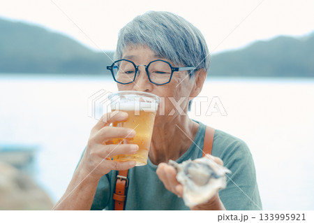 シニア女性が海辺でビールと牡蠣を楽しむシーン 133995921