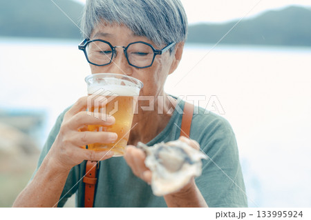 シニア女性が海辺でビールと牡蠣を楽しむシーン 133995924