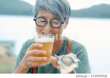 シニア女性が海辺でビールと牡蠣を楽しむシーン シニア女性が海辺でビールと牡蠣を楽しむシーン 133995926