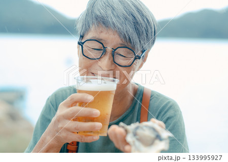 シニア女性が海辺でビールと牡蠣を楽しむシーン 133995927