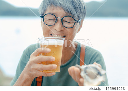 シニア女性が海辺でビールと牡蠣を楽しむシーン 133995928
