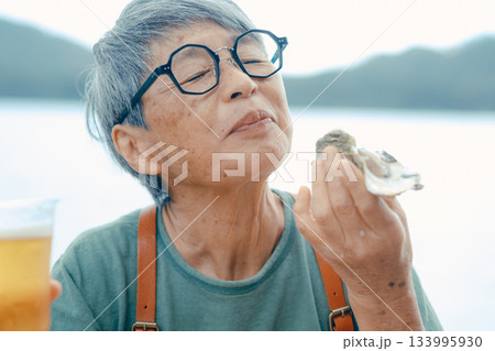 シニア女性が海辺でビールと牡蠣を楽しむシーン 133995930