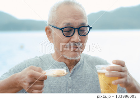 シニア男性が海辺でビールと貝料理を楽しむシーン 133996005