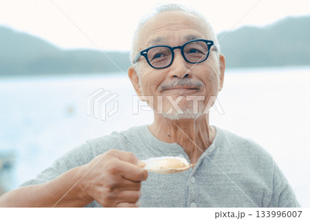 シニア男性が海辺でビールと貝料理を楽しむシーン 133996007