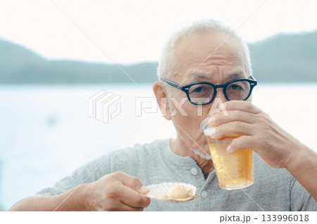 シニア男性が海辺でビールと貝料理を楽しむシーン 133996018