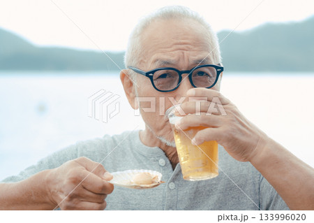 シニア男性が海辺でビールと貝料理を楽しむシーン 133996020