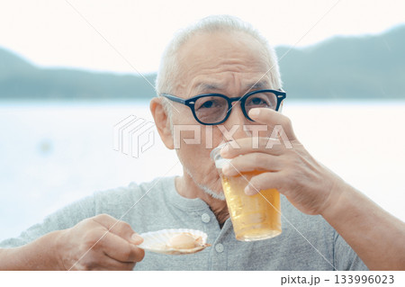 シニア男性が海辺でビールと貝料理を楽しむシーン シニア男性が海辺でビールと貝料理を楽しむシーン 133996023