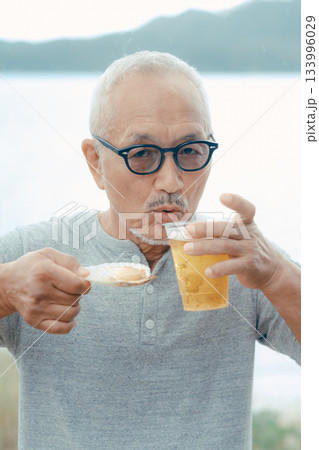 シニア男性が海辺でビールと貝料理を楽しむシーン 133996029