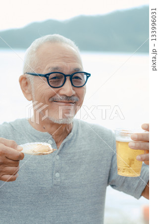 シニア男性が海辺でビールと貝料理を楽しむシーン 133996031