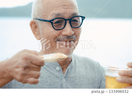 シニア男性が海辺でビールと貝料理を楽しむシーン 133996032