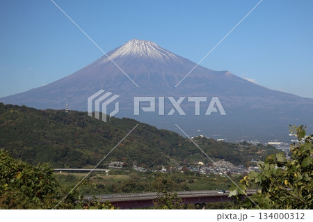 青空と冠雪した富士山と山並みと街並みと高速道路橋のある風景 134000312
