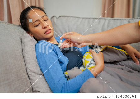 A Woman Resting on a Couch with a Fever Being Cared For by Someone Close by A Woman Resting on a Couch with a Fever Being Cared For by Someone Close by 134000361