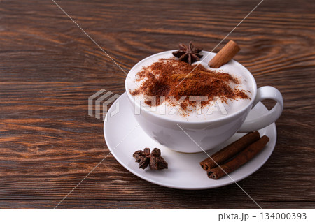 Pumpkin Spice Latte pumpkin drink topped with whipped cream sits in a white cup. Surrounding it pumpkins and cinnamon sticks creating a festive fall atmosphere. Pumpkin Spice Latte pumpkin drink topped with whipped cream sits in a white cup. Surrounding it pumpkins and cinnamon sticks creating a festive fall atmosphere. 134000393