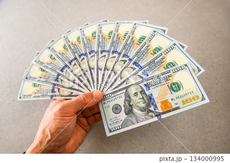 米100ドル紙幣12枚を扇状に広げ左手で手前から奥へ差し出すぼかし気味 134000995
