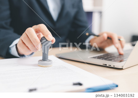Businessman signing and stamping official document at desk, concept of legal contract approval, authorization or business agreement confirmation in corporate office background. stamp approval 134003192