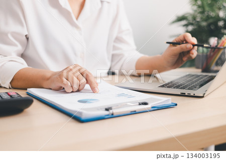 Close up of businessperson analyzing financial chart and graph with pen and calculator on desk, concept of accounting management, budget planning, financial report and data analysis. Close up of businessperson analyzing financial chart and graph with pen and calculator on desk, concept of accounting management, budget planning, financial report and data analysis. 134003195