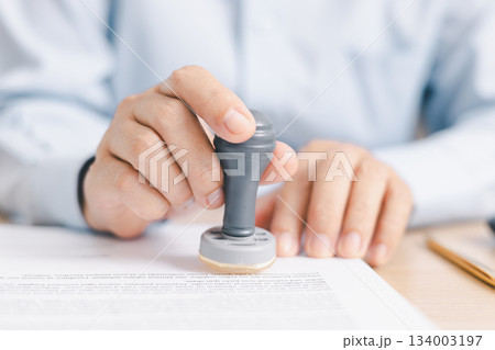 Businessperson stamping document on clipboard at office desk, concept of contract approval, legal authorization, business agreement validation or administrative paperwork process. stamp approval. 134003197
