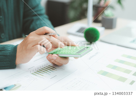 Close-up of hand using green calculator on financial charts with eco earth globe, symbolizing sustainable finance, green business planning, environmental accounting and clean economic growth. Close-up of hand using green calculator on financial charts with eco earth globe, symbolizing sustainable finance, green business planning, environmental accounting and clean economic growth. 134003337